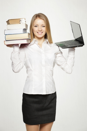 Young female holding heavy stack of books in one hand and laptop in another, isolated on gray backgroundの写真素材