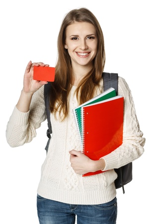 Happy young woman wearing a backpack and holding notebooks showing blank credit card, over white background  Student loan concept の写真素材