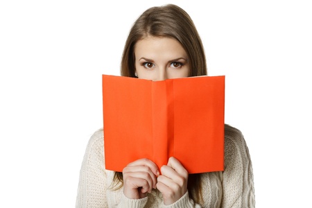 Closeup of young woman peeking over the edge of the opened book, looking at camera, over white backgroundの写真素材