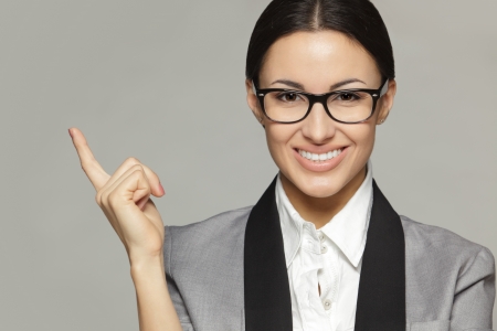 Closeup of young business woman in eyeglasses pointing at copy space, over grey backgroundの写真素材