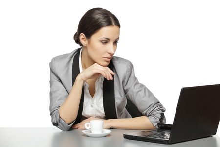 Serious business woman reading at laptop screen sitting at her work desk, isolated on white backgroundの写真素材