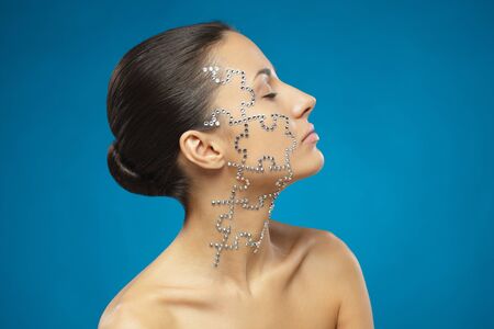 Side view portrait of female with beauty crystal puzzle on her face, over blue backgroundの写真素材