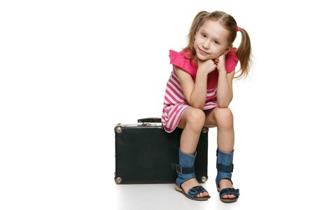 Little tourist  Little girl with sitting on the old fashioned suitcase in full length, over white backgroundの写真素材