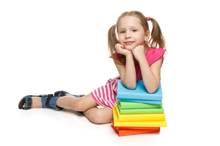 Smiling little girl sitting on the floor leaning on the stack of books, over white backgroundの写真素材