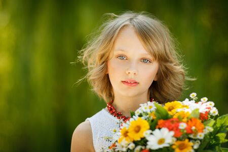 Girl with bunch of flowers standing outdoors over green backgroundの写真素材