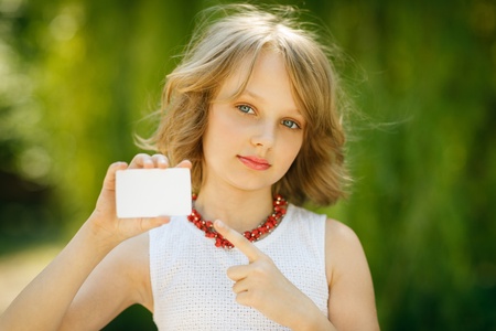 Girl showing blank credit card and pointing at it standing outside, over green grass backgroundの写真素材
