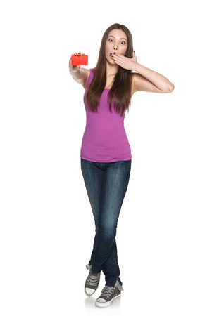 Surprised young teen female showing blank credit card with hand over mouth in full length against white backgroundの写真素材