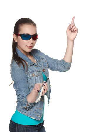 Young female wearing 3D glasses holding a TV remote control, pointing up at blank copy space, isolated on whiteの写真素材