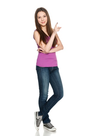 Lovely teen girl in full length standing casually and pointing to the side at blank copy space, against white backgroundの写真素材