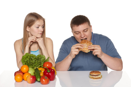 Choosing healthy eating concept  Surprised woman looking her boyfreind eating fast food, against white backgroundの写真素材
