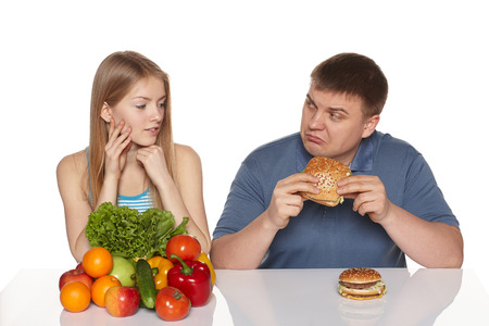 Choosing healthy eating concept  Woman looking whit dissaproval look as her boyfriend eating fast food, against white backgroundの写真素材