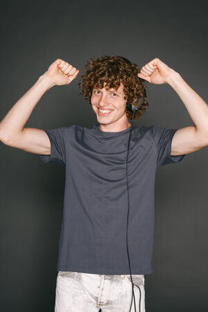 Happy winner man with headphones celebrating success with hands raised, aganst gray backgroundの写真素材