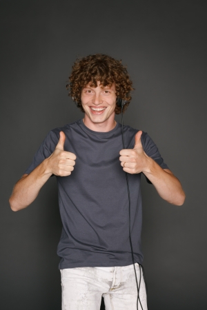 Happy male in headphones gesturing thumb up, against gray backgroundの写真素材