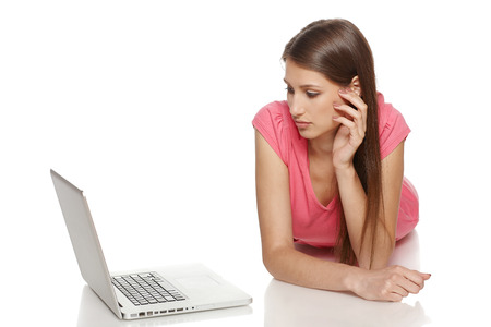 Concentrated casual young female lying on the floor, looking at the laptop screen, isolated on whtie backgroundの写真素材