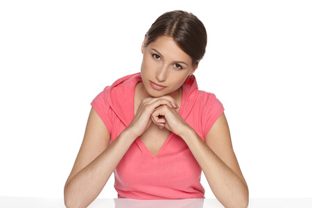 Pensive young female sitting at white table leaning on her elbows, isolated on white backgroundの写真素材