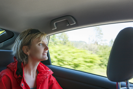 Traveling by car. Smiling woman enjoying the  trip, looking throught the car window, motion blur background. Road trip travel vacation. の写真素材