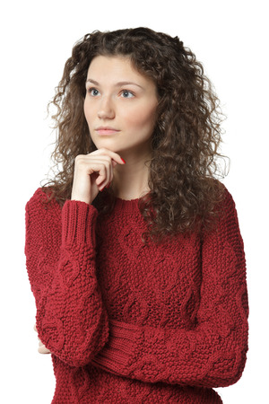 Portrait of young pensive female standing with folded hands and her hand on the chin looking sideways, over white backgroundの写真素材