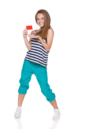 Positive teen girl hipster in casual summer clothes standing in full length and showing blank credit card, over white backgroundの写真素材