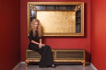 Fashion model in long black dress posing in glamorous red interiorの写真素材