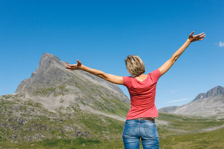 Back view of happy woman enjoying freedom with arms outspread enjoying peace, serenity in nature outdoors, in top of mountains, Norwayの写真素材