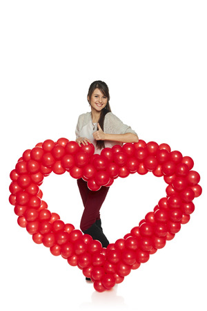 Love concept. Full length smiling woman holding red balloon heart isolated on white background.  Cute young woman in love.の写真素材