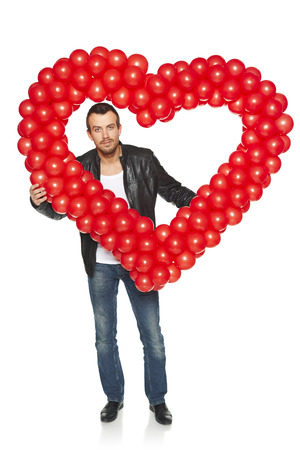 Love concept. Full length dude man peeping through the heart shape formed of d balloons, isolated on white .の写真素材