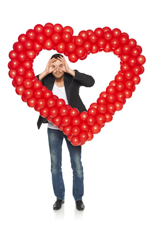 In search of love concept. Man looking through circled fingers through heart shape, isolated on white background.の写真素材