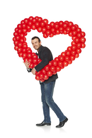 Love concept. Full length handsome man carrying heart shape formed of d balloons, isolated on white .の写真素材