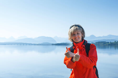 Woman tourist in Norway showing thumbs up against blue hazy mountains backgroundの写真素材