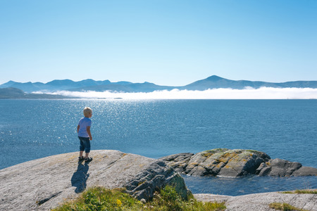Norwegian landscape back view of a little boy enjoying view at fjord Kvernesfjorden with clouds floating over waterの写真素材