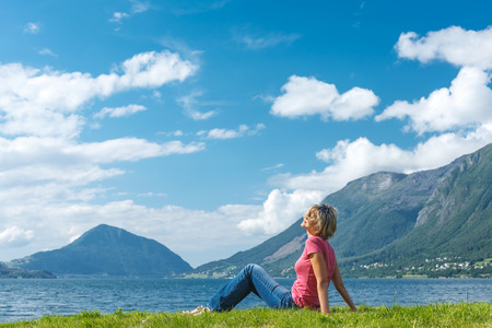 Woman relaxing enjoying at the fjord coast in a summer sunny day, Norwayの写真素材