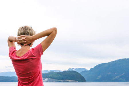 Back view of a woman enjoying a view at fjord with hands over headの写真素材