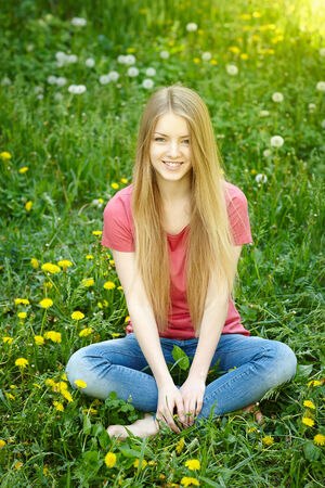 Smiling female sitting on the field of dandelions looking at camera, spring female portraitの写真素材
