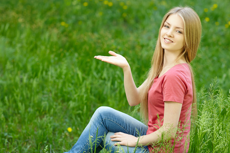 Woman sitting outdoors on green meadow holding blank copy space on her open palmの写真素材
