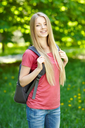 Portrait of young smiling woman student with backpack on green background of city parkの写真素材