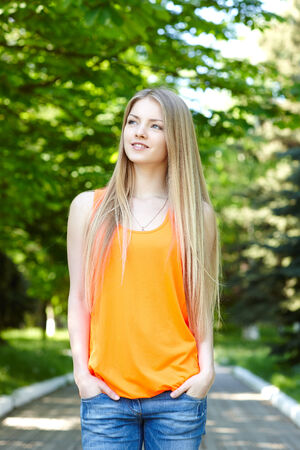 Summer girl portrait.  Pensive casual woman standing with hands in pockets smiling happy on sunny summer or spring day outside in park, looking away. Pretty young woman outdoors.の写真素材