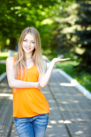 Woman smiling happy on sunny summer or spring day outside in park holding blank copy space on her open palm. Pretty young woman outdoors.の写真素材