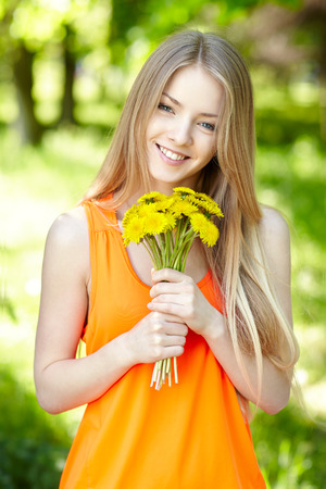 Spring girl. Lovely blond girl with bunch of dandelions outdoors.の写真素材