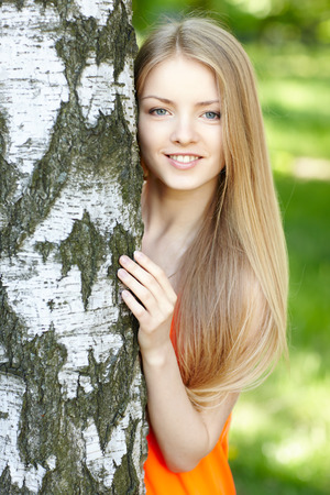 Beautiful female peeping from behind tree, against green of summer park.の写真素材
