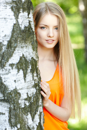 Beautiful female peeping from behind tree, against green of summer park.の写真素材