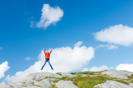 Woman hiker jumping for joy on stones in Norway, remote viewの写真素材