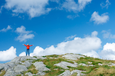 Remote view of happy excited woman hiker standing on wild nature of Norway with raised hands wavingの写真素材