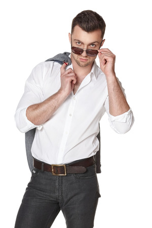 Stylish businessman with jacket over shoulder peering over the rim of sunglasses isolated on whiteの写真素材