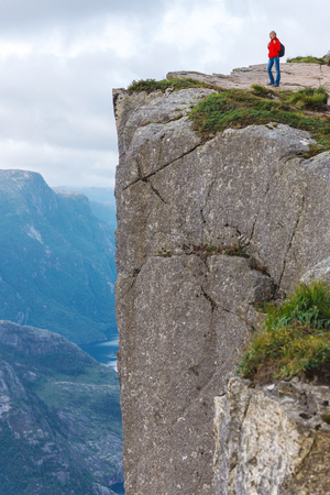 Woman hiker standing on cliff of Pulpit Rock / Preikestolen, Norway. Pulpit rock is a massive cliff 604 metres above Lysefjorden, almost flat, and is a famous tourist attraction in Norway.の写真素材