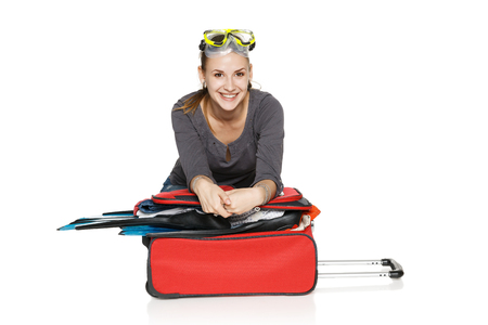 Happy female packing her suitcase for summer vacations, isolated on white の写真素材