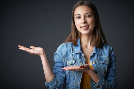 Portrait of stylish denim teen female showing / holding blank copy space on the palm or welcoming, over dark studio の写真素材
