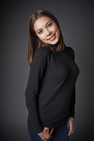 Portrait of smiling candid playful teen female over dark studio の写真素材