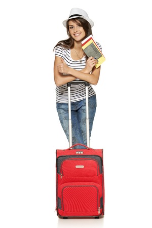 Full length of young female in casual standing with travel suitcase, holding passport and tickets and gesturing thumb up, isolated on white の写真素材
