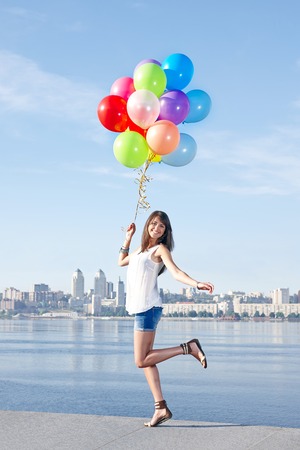 Happy young woman with colorful balloons in full length jumping, urban scene, outdoorsの写真素材