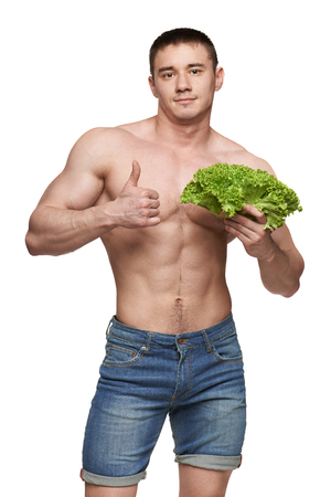 Fit young male holding vegetables and showing thumbs up, isolated on white backgroundの写真素材